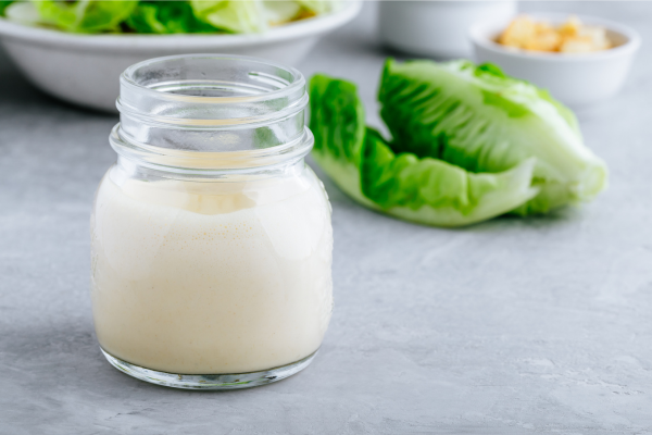 a clear glass jar of creamy dressing, romaine lettuce in the background